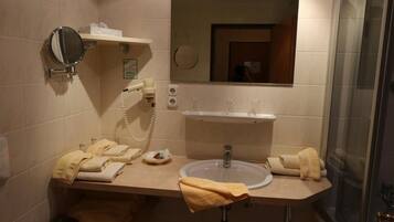 A bathroom with a sink, mirror, and hairdryer. There are towels on the counter.