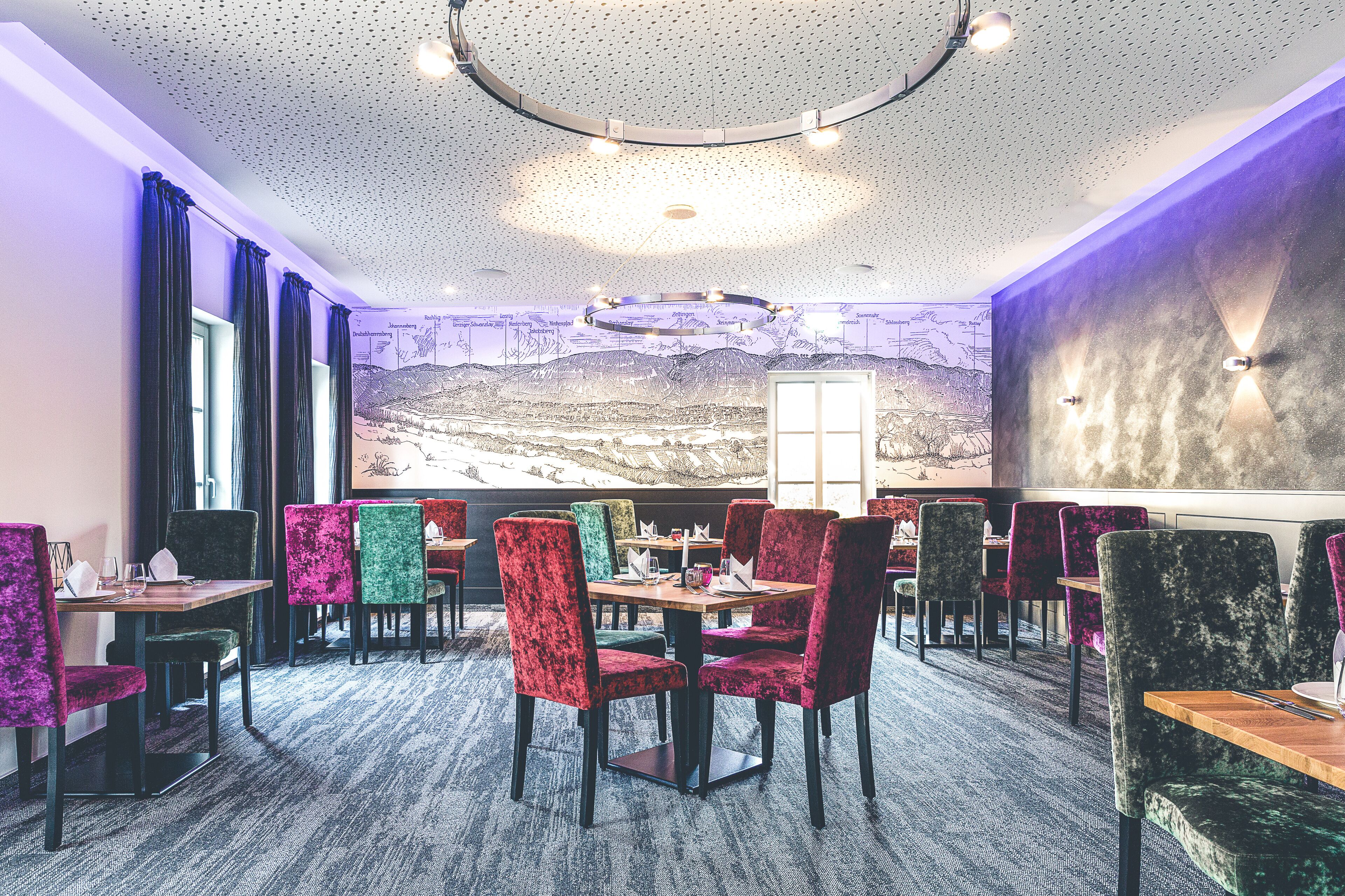 A restaurant with round tables and colorful chairs, a mural on the wall, and a ceiling with a circular light fixture.