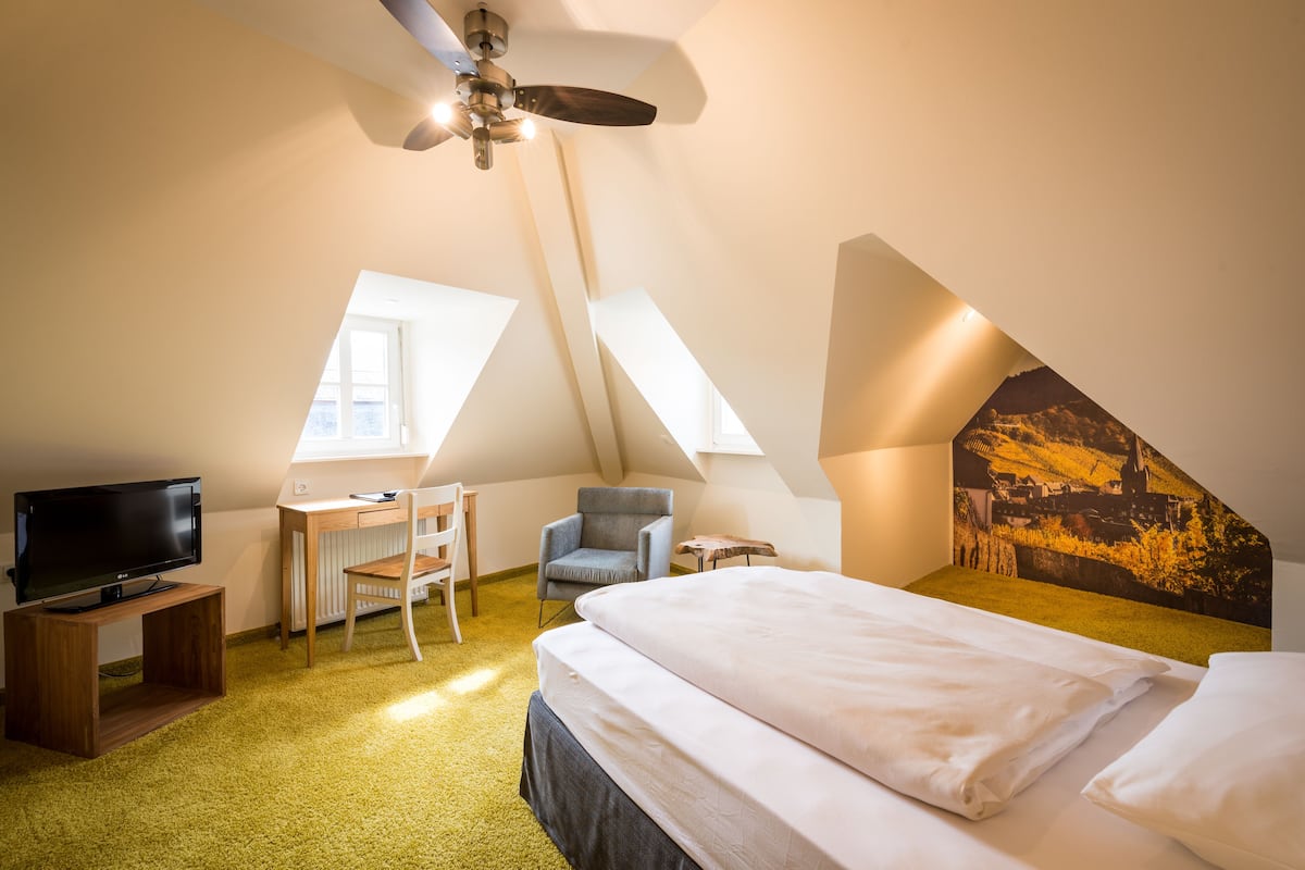 A bedroom with a bed, a desk, a chair, a television, and a ceiling fan.