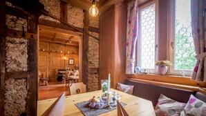 A rustic wooden dining area with a table set for two, a stone wall, and a window with a view of greenery.