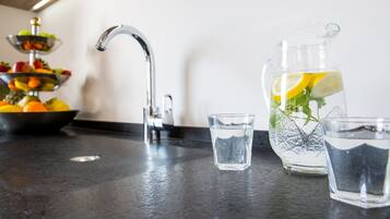 Una encimera de cocina con un frutero, una jarra de agua con rodajas de limón y dos vasos.
