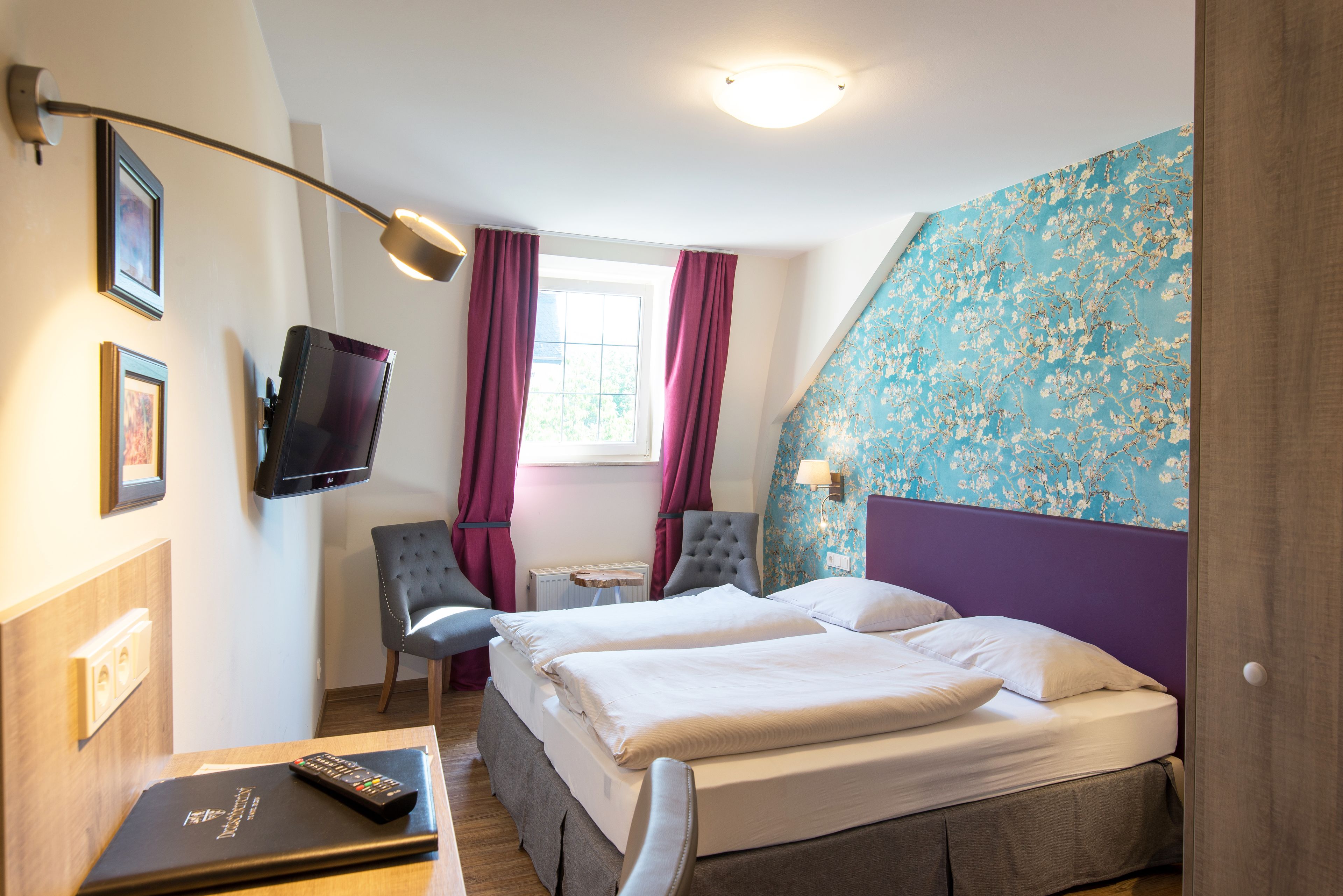 Ein Hotelzimmer mit zwei Betten, einem Fernseher, einem Schreibtisch und einem Sessel.
