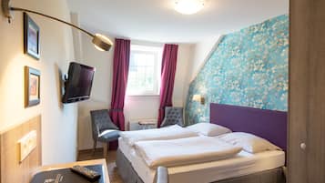 Ein Hotelzimmer mit zwei Betten, einem Fernseher, einem Schreibtisch und einem Sessel.