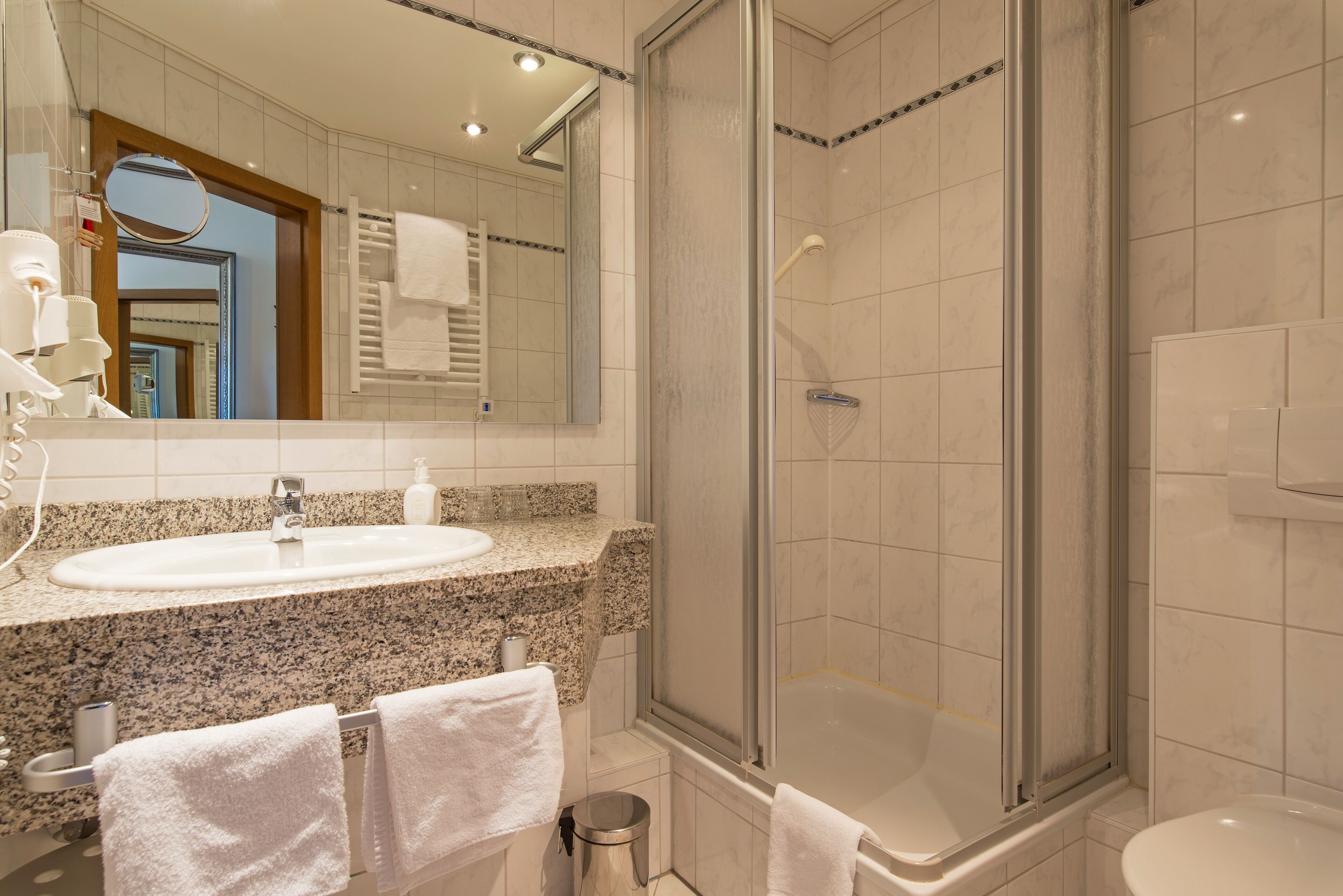 A modern bathroom with a granite countertop sink, a glass shower enclosure, and a toilet.