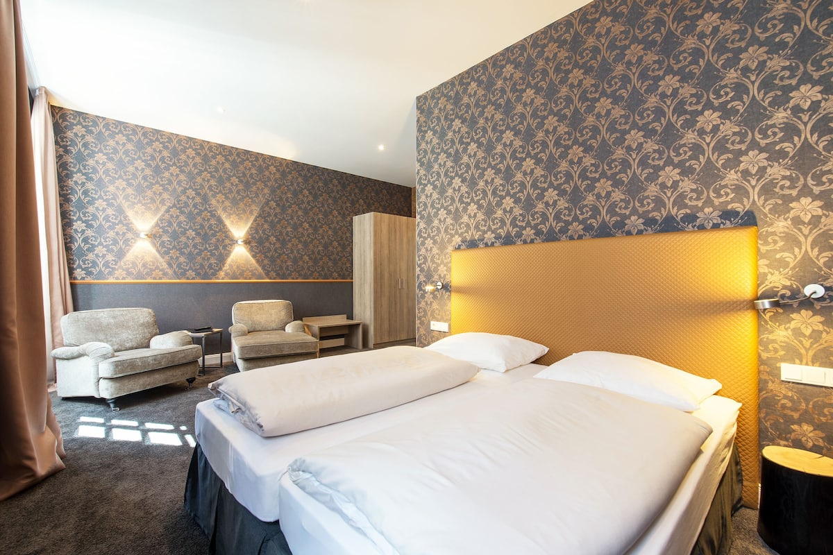 A hotel room with two beds, a sofa, a chair, and a wardrobe.