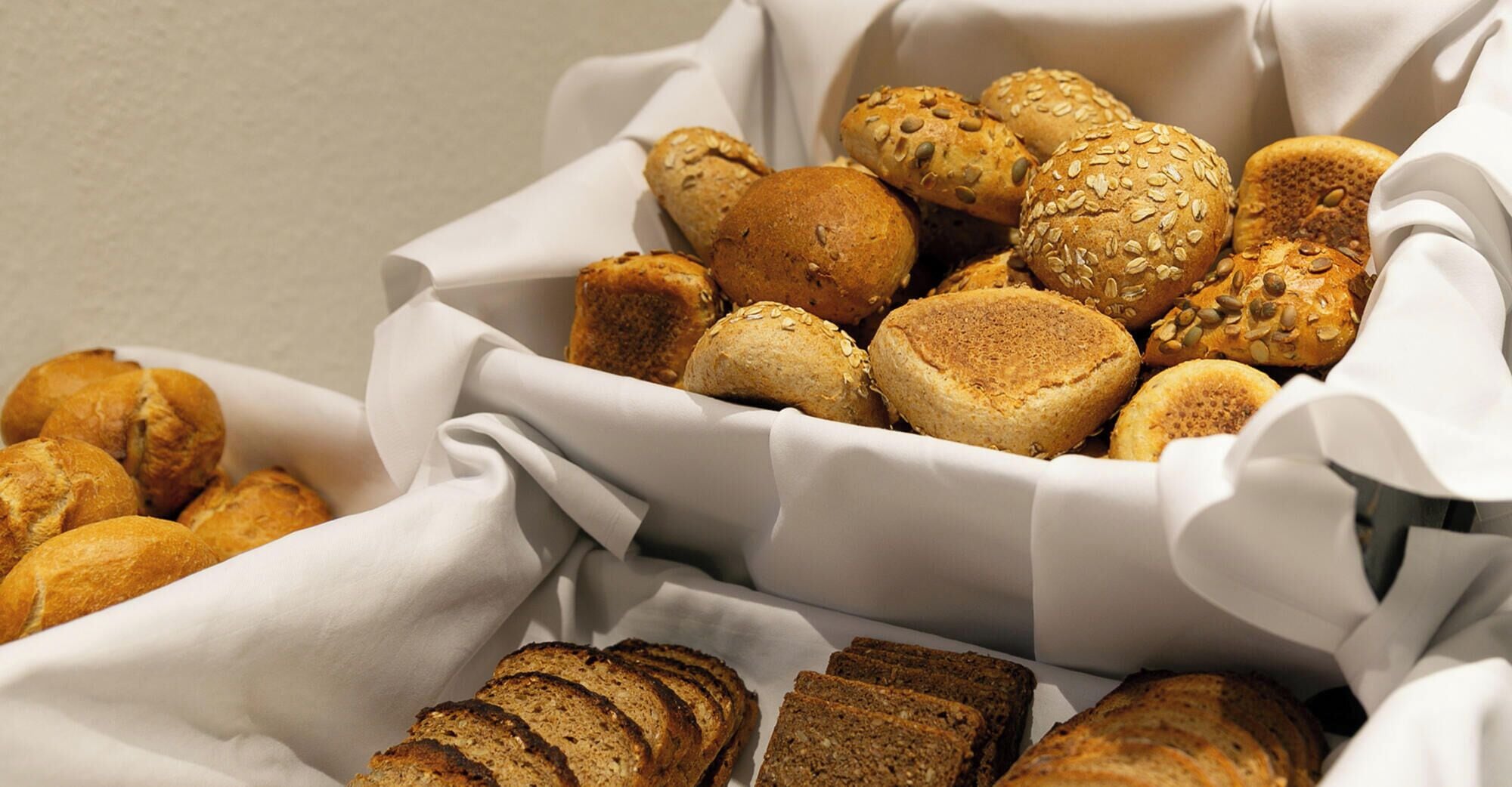 A basket of various breads and rolls, including seeded and sliced varieties.
