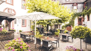 An outdoor café with tables and chairs, surrounded by potted plants and a stone wall.