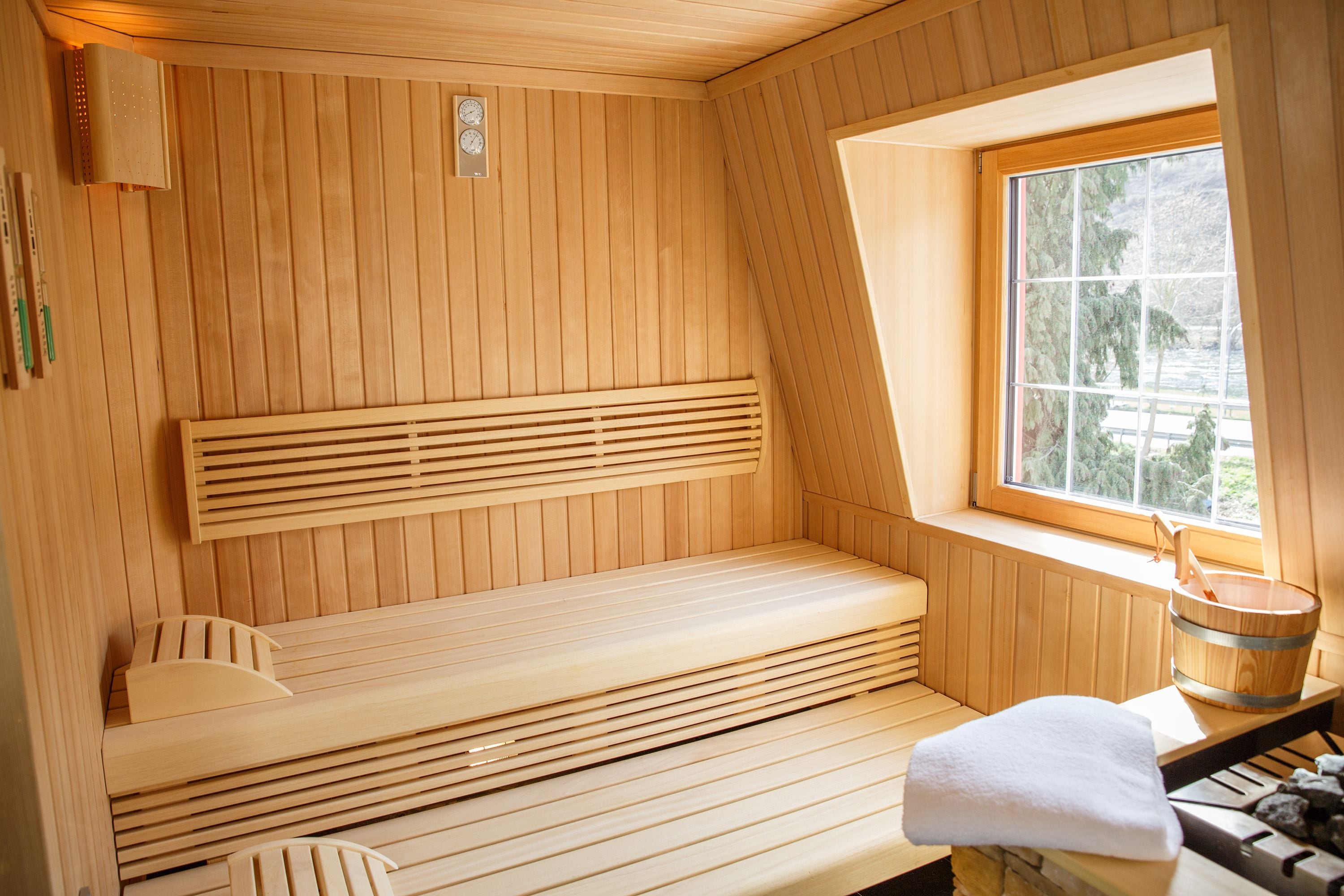 A wooden sauna with benches, a window, and a wooden bucket.