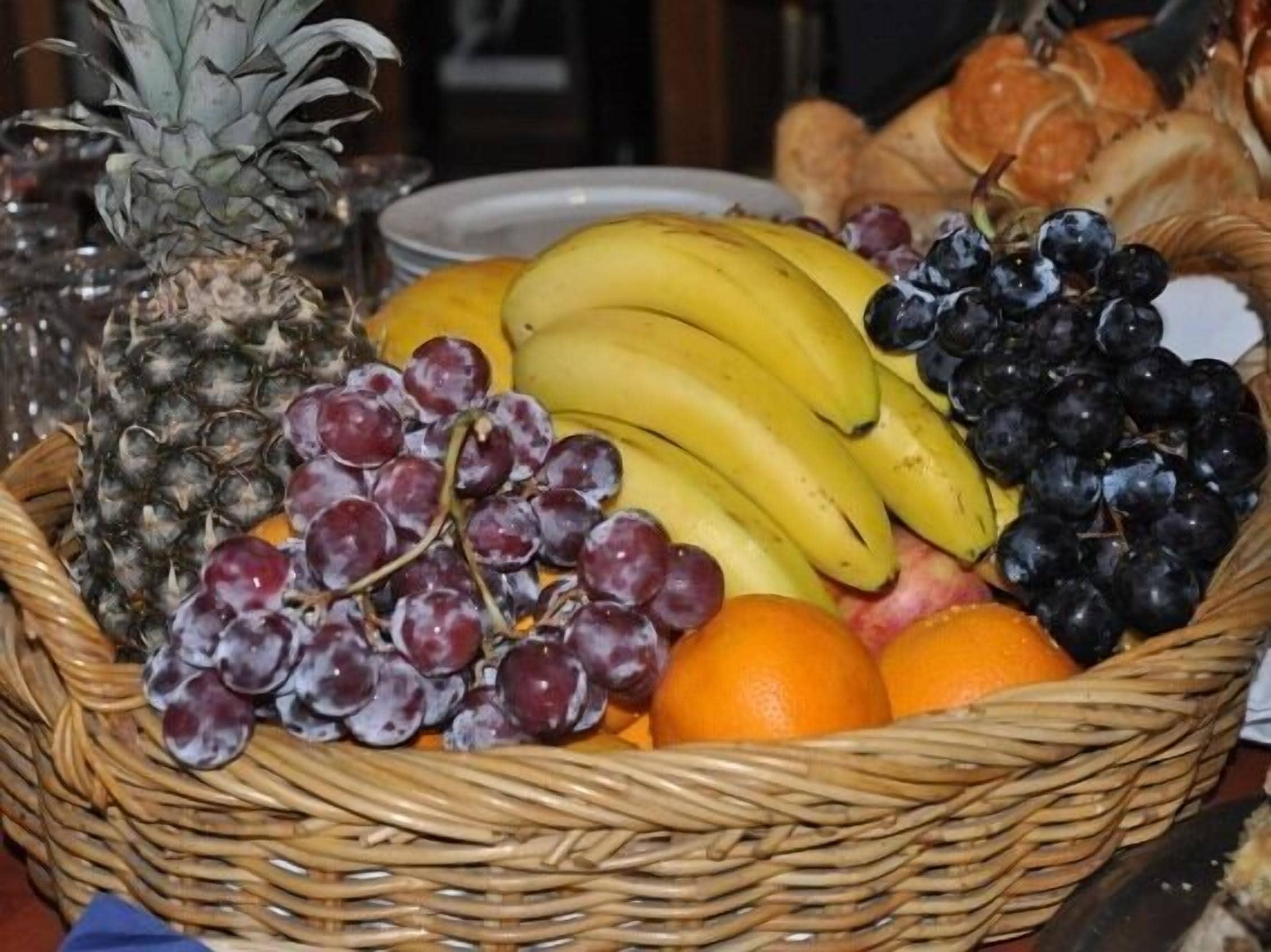 A wicker basket containing a pineapple, bananas, grapes, oranges, and bread.