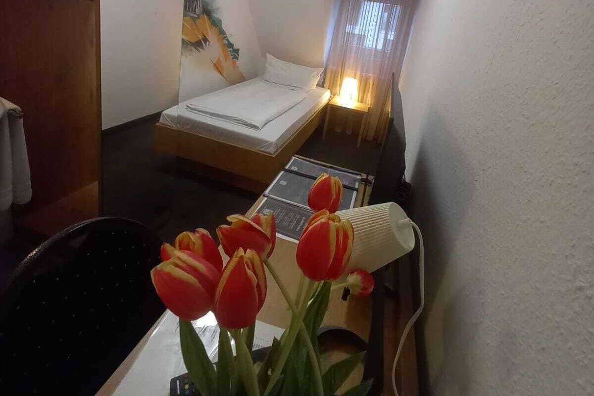 A small, cozy room with a bed, a desk with a lamp, and a window with curtains.