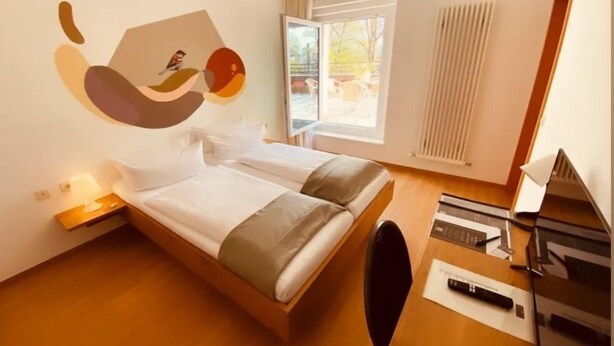 Ett modernt hotellrum med en säng, ett skrivbord och ett stort fönster.