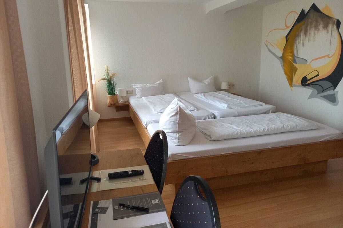 A bedroom with a bed, a desk, a chair, a TV, and a wall painting.