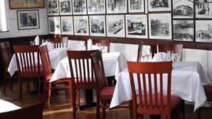En restauranginteriör med flera bord och stolar, inramade fotografier på väggen och ett trägolv.