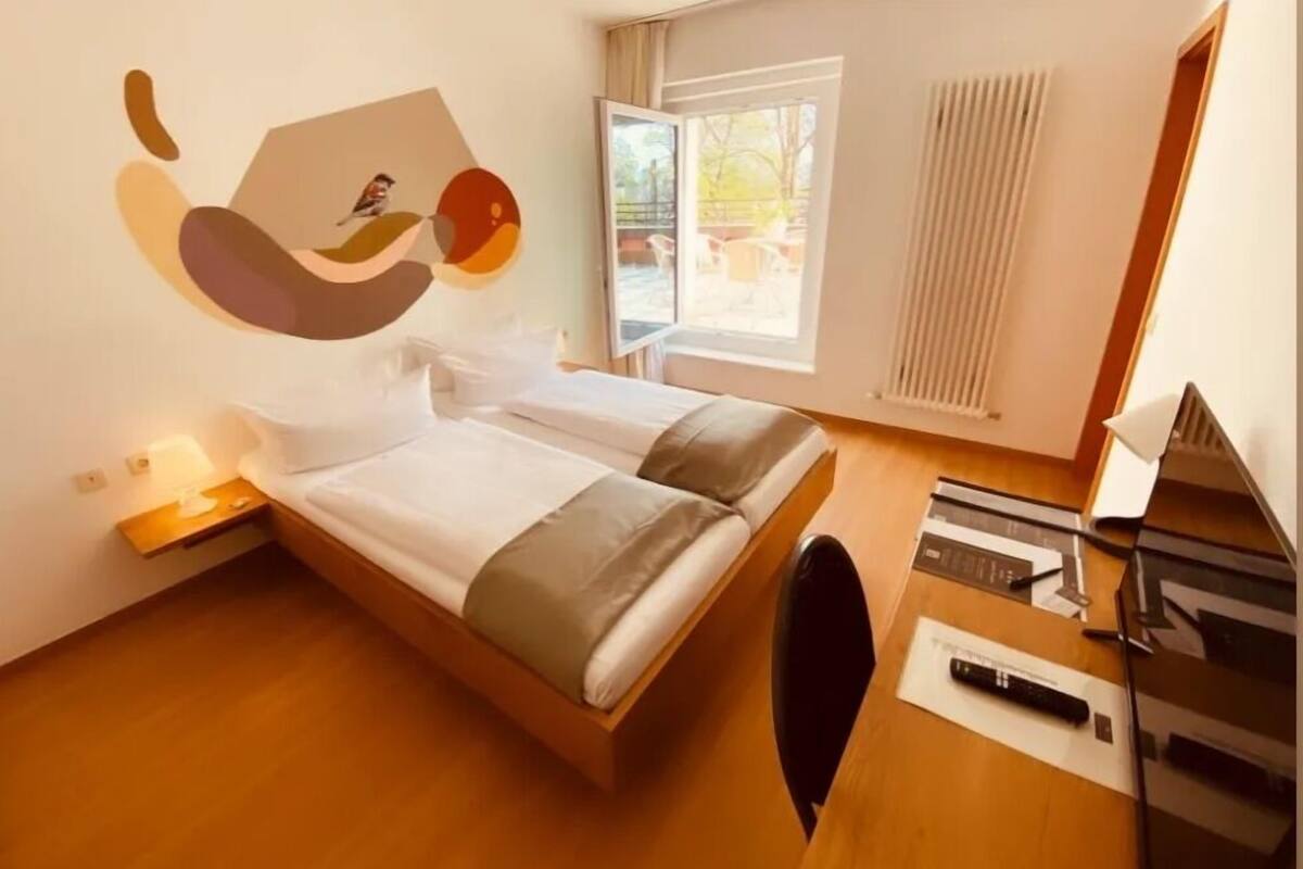 A modern hotel room with a bed, a desk, and a view of the outdoors.