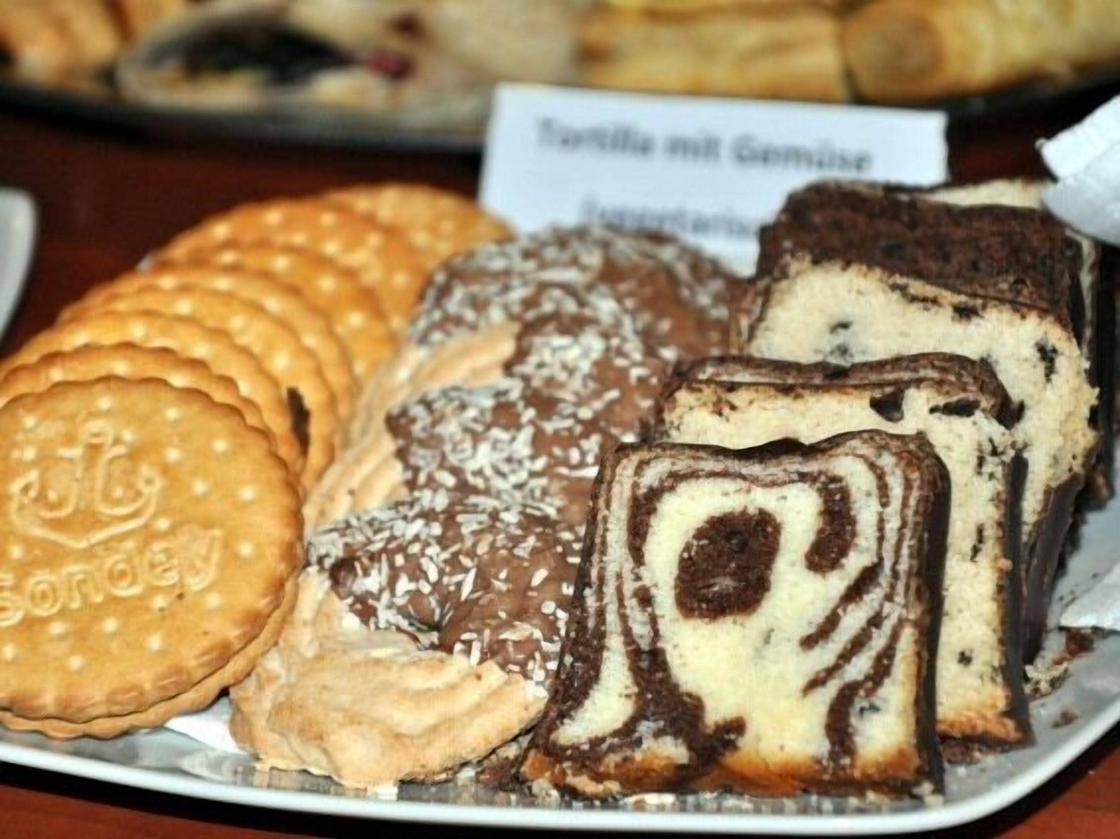 Een bord met diverse gebakjes, waaronder een chocoladerol, een stuk taart en ronde koekjes.