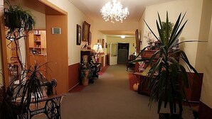 A hallway with a chandelier, potted plants, and a wooden cabinet. - Landhotel Peters (Wustrow)