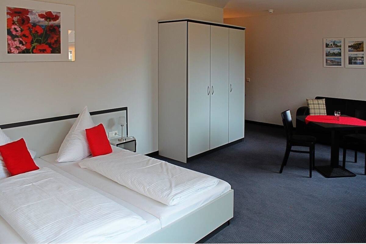 Ett hotellrum med två sängar, en garderob, ett matbord med stolar och konstverk på väggarna.