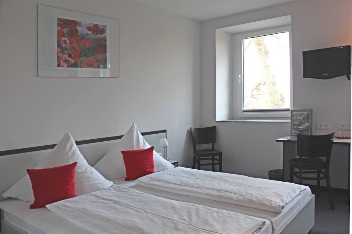 Ett hotellrum med två sängar, ett skrivbord, en stol, en TV och ett fönster med utsikt.
