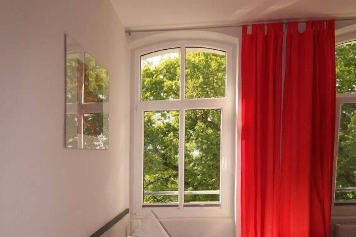 Ett hotellrum med en säng, ett fönster med utsikt över träd och en röd gardin.