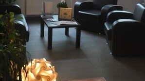 Una habitación con dos amplios ventanales de arco, un sofá de color oscuro, una pequeña mesa y una planta en maceta.