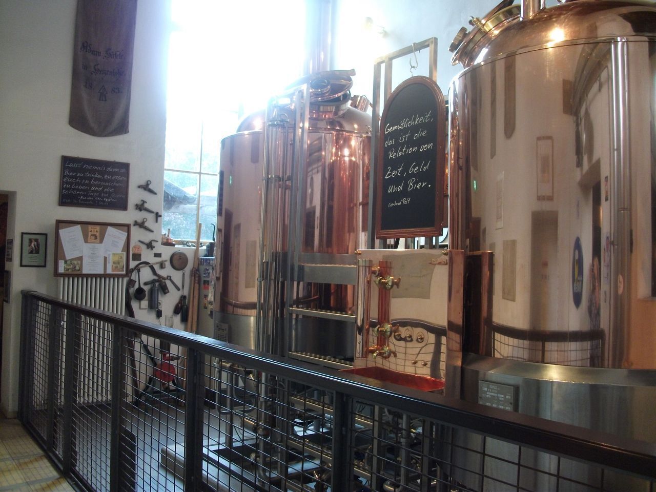 A brewery with stainless steel brewing equipment, a chalkboard with brewing instructions, and a view of the outside through a window.