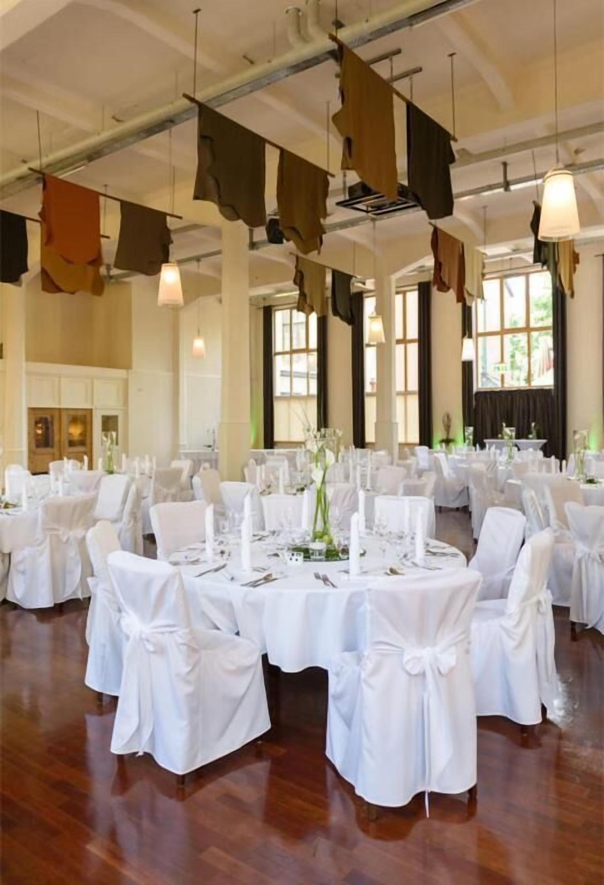 A banquet hall with round tables set for dining, white chairs, and hanging fabric decorations.