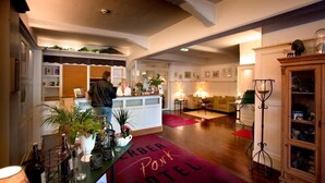 A hotel lobby with a reception desk, a red carpet with "Caber Park Hotel" text, a sofa, and a cabinet with glass doors. - Gerber Park Hotel (Uhingen)