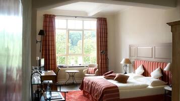 A hotel room with a large bed, a small table, a chair, and a window with curtains.