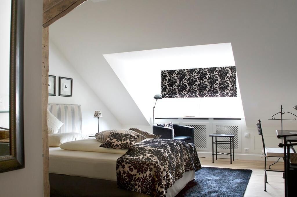 Un dormitorio con cama, escritorio y ventana con persiana estampada.