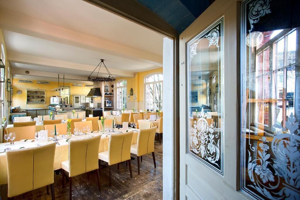 A dining area with tables set for service, a kitchen in the background, and a decorative window with intricate patterns.