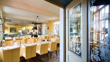 A dining area with tables set for service, a kitchen in the background, and a decorative window with intricate patterns.
