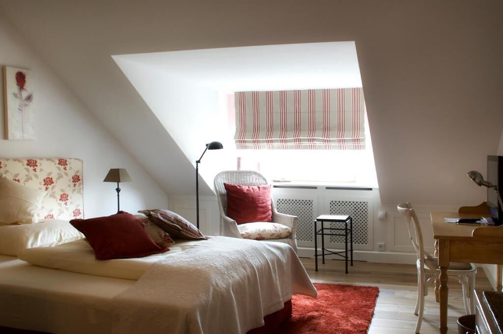Un dormitorio con cama, una silla, un escritorio y una ventana con cortinas a rayas.