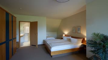 Hotelkamer met een groot bed, een houten kledingkast, een badkamer met wastafel en spiegel, en een potplant.