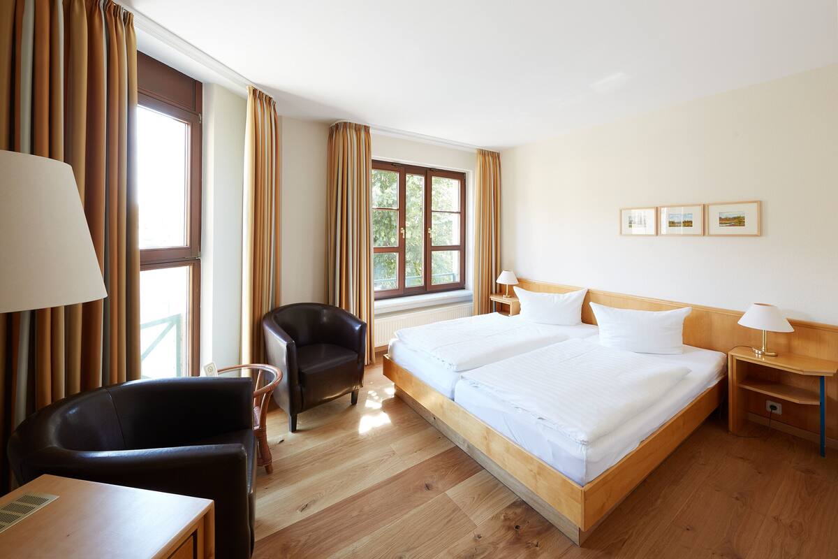 A hotel room with a wooden bed, a desk, a chair, and a window with curtains.