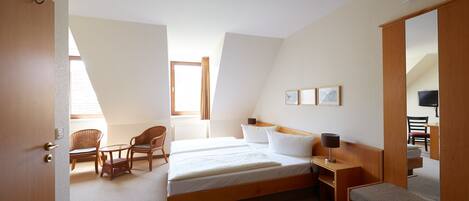 A hotel room with a large bed, two chairs, a small table, a bench, and a TV.