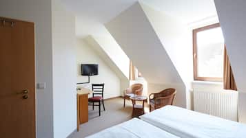 Ein Hotelzimmer mit Bett, Schreibtisch mit Stuhl, Fernseher und einem Fenster mit Vorhängen.