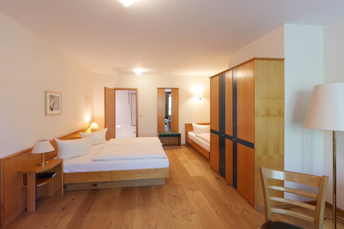 A hotel room with a wooden bed, bedside tables, a wardrobe, and a chair.