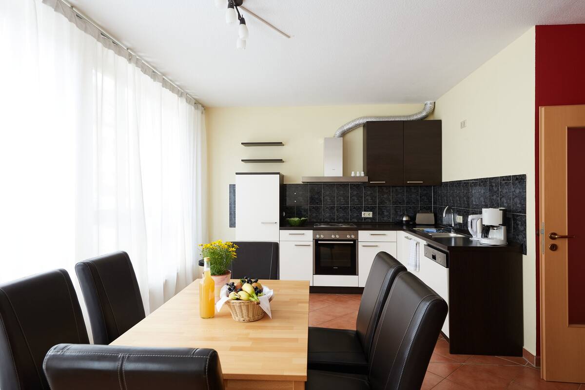 A modern kitchen with a dining area, featuring a wooden table, black chairs, and a kitchen island with a sink and stove.