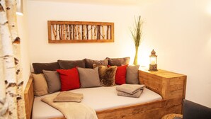 A cozy wooden sofa bed with multiple cushions, a decorative wall piece, and a small table with a lantern. - Pension Sommer (Waldsassen)