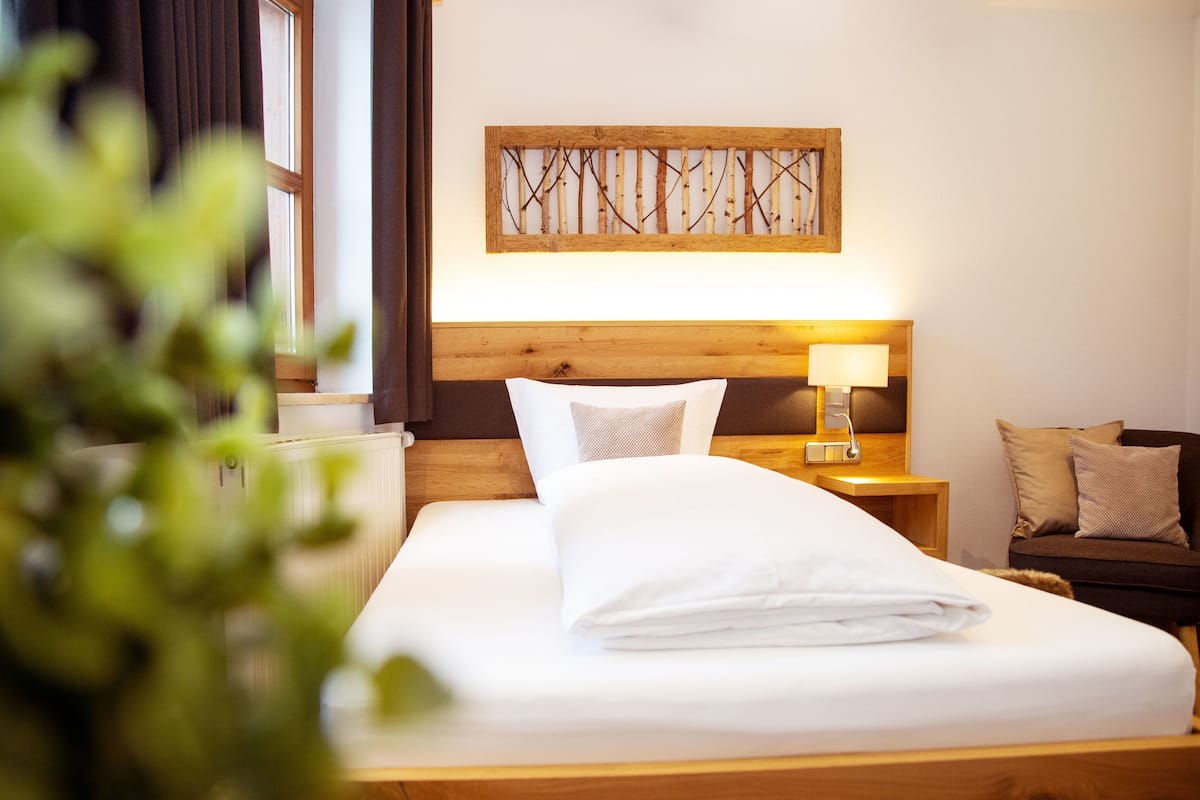 A neatly made bed with white linens, a wooden headboard, a bedside lamp, and a wall-mounted artwork.
