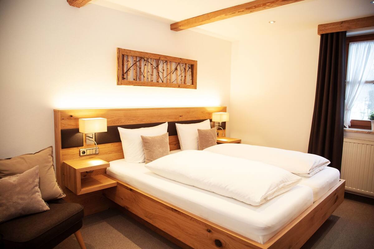 A hotel room with a wooden bed, bedside lamps, a headboard with a branch design, and a window with curtains.