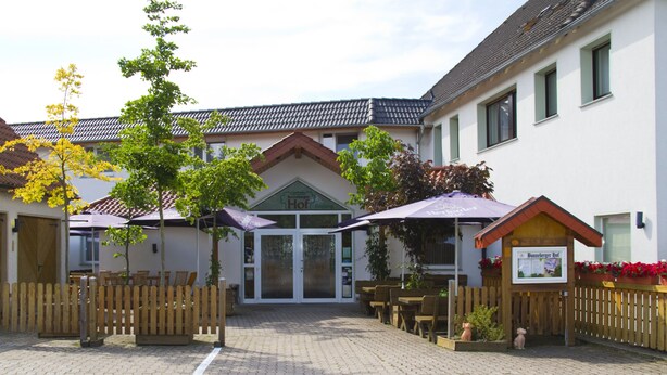Une cour avec des sièges en plein air, une clôture en bois et un bâtiment sur lequel on peut lire l’inscription « Hof ».