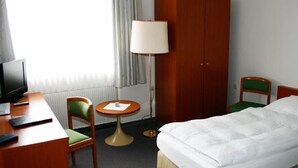 Une chambre d’hôtel comprenant un lit, un bureau avec un ordinateur, une chaise, une petite table ronde et une lampe.