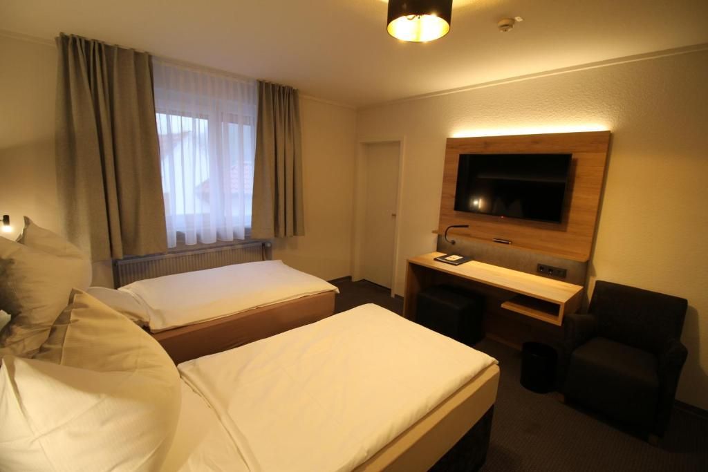 A hotel room with two beds, a desk, a chair, a television, and a window with curtains.