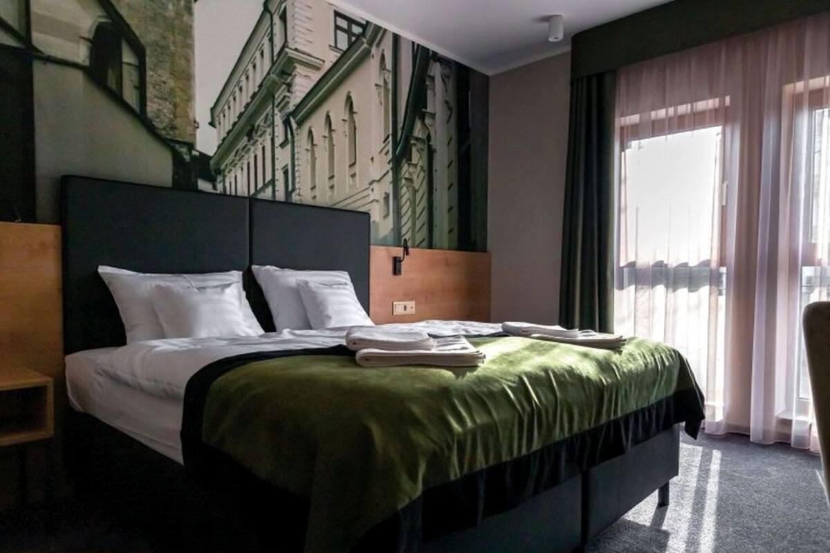 A hotel room with a large bed, a headboard, a nightstand, a window with curtains, and a wall mural.