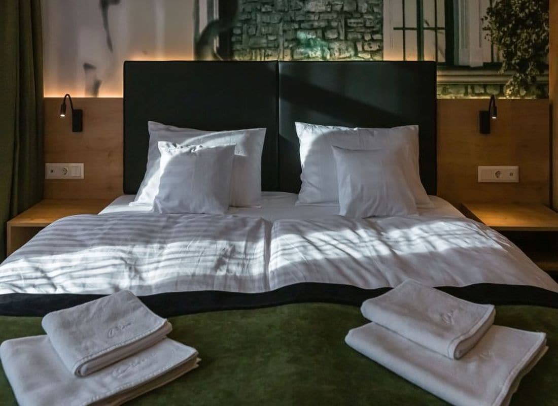 A neatly made bed with white linens, two pillows, and folded towels on a green bedspread.