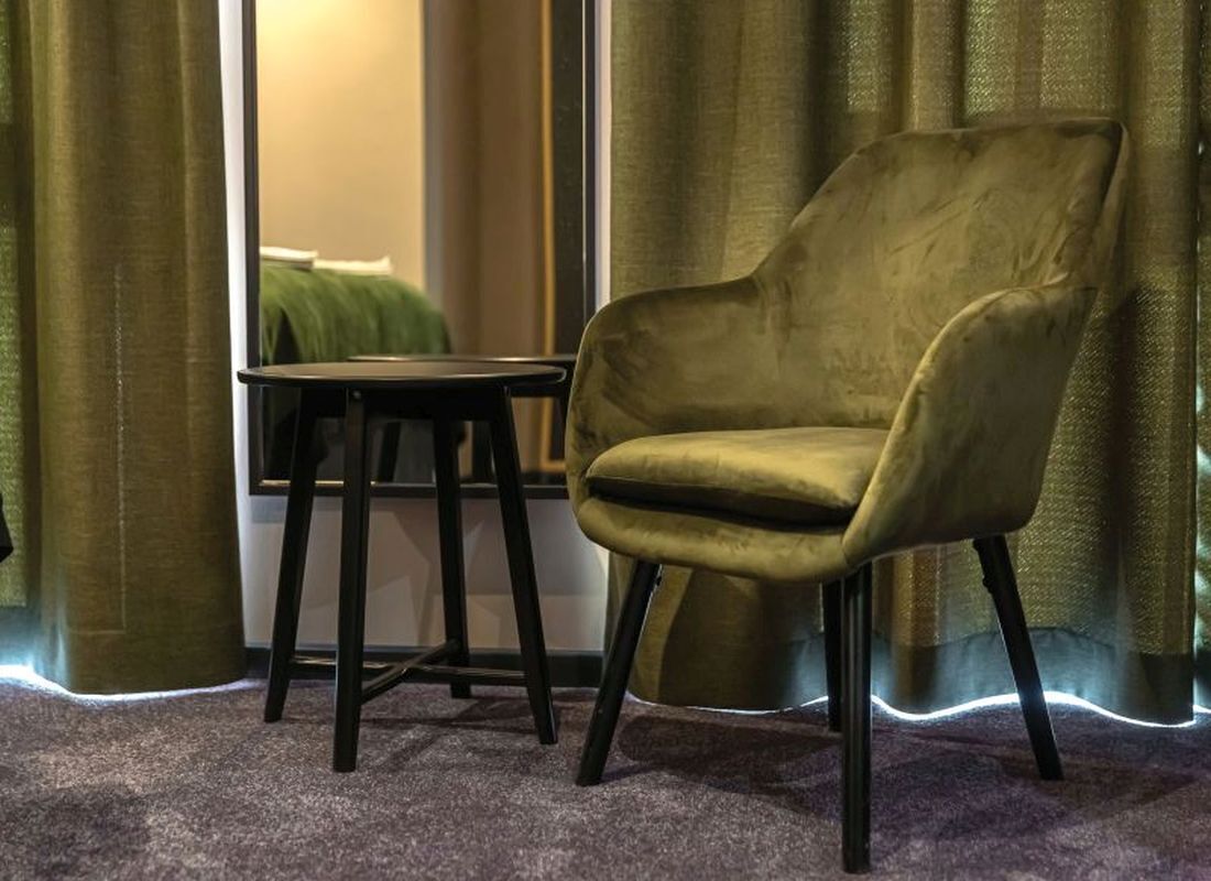 A room with a green armchair, a small table, and a mirror.
