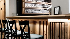 A bar area with wooden slats, black chairs, and shelves of glasses.