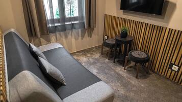 Un salón moderno con un sofá, dos mesitas redondas, una planta en maceta y un televisor montado en la pared.