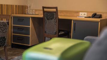 Habitación pequeña con un escritorio de madera, una silla, un mueble bajo y un objeto verde en primer plano.
